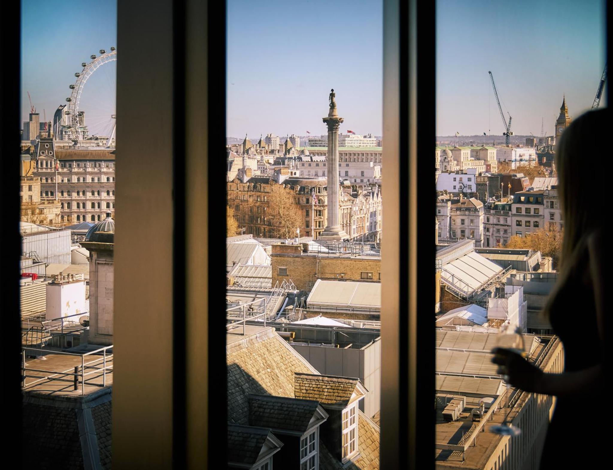 a woman looking out a window at a city at The Londoner in London