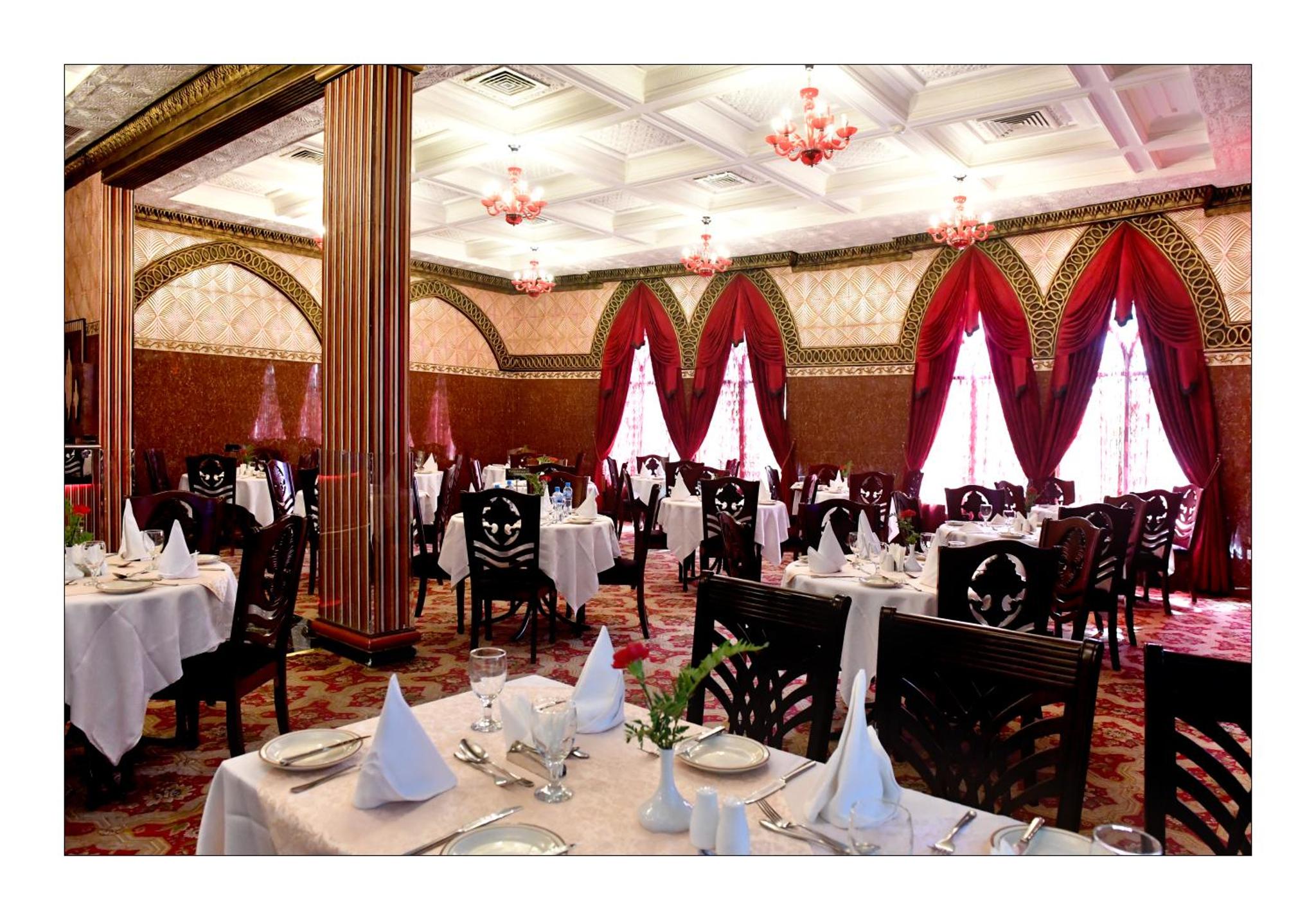 a dining room with tables and chairs and red curtains at Gulf Gate Hotel in Manama