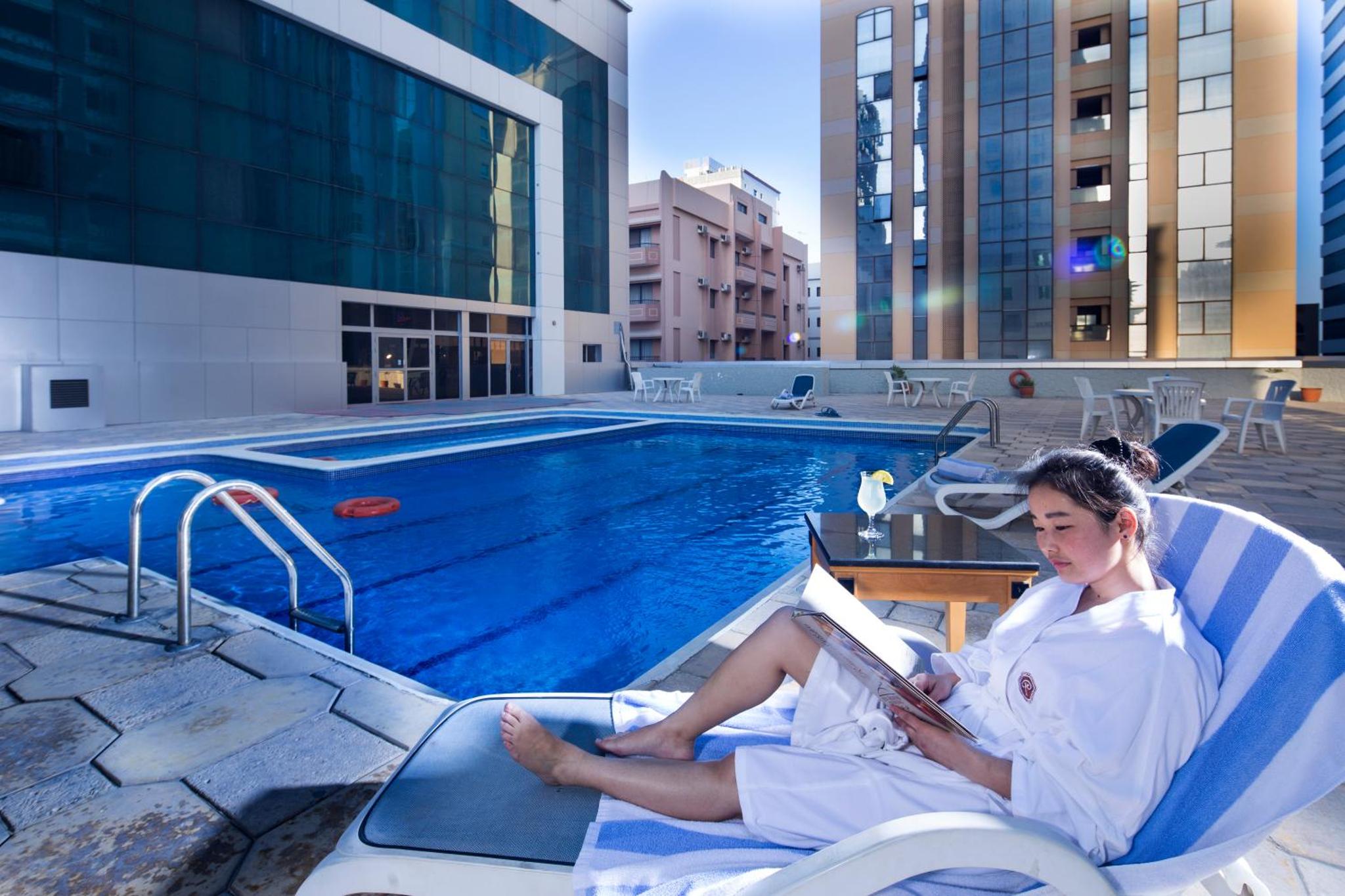 a woman sitting in a chair reading a book next to a swimming pool at Baisan International Hotel in Manama