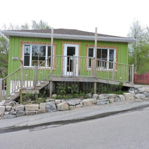 a small green house with a porch and rocks at Tadou-Shack in Tadoussac