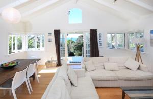 een woonkamer met een witte bank en een tafel bij Cape Cottage in Oneroa