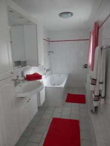 Baño blanco con bañera blanca, lavamanos y alfombra roja en Ferienwohnung Nessler, en Radebeul