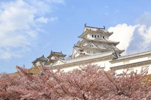 a tall white building withakura trees in front of it at Hotel Monterey Himeji in Himeji