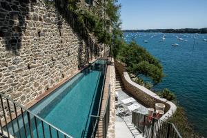 ein Pool neben einer Steinmauer neben dem Wasser in der Unterkunft Castelbrac Hotel & Spa in Dinard