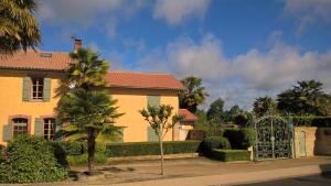 a yellow house with a gate and palm trees at Cote jardin in Hontanx