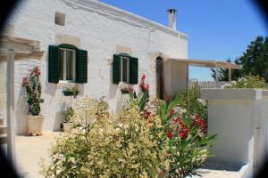 a white building with green shuttered windows and flowers at Casolare Capitolo in Cisternino