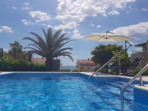 a swimming pool with an umbrella and a palm tree at Apartments Diamond in Podstrana
