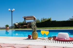 a pineapple and two glasses of juice next to a swimming pool at Villa Elisabeth in Perama