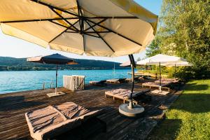 a wooden deck with chairs and umbrellas on the water at Seevillen Excelsior in Velden am Wörthersee