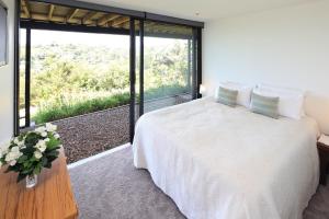 a bedroom with a white bed and a large window at Blackwood Retreat in Oneroa