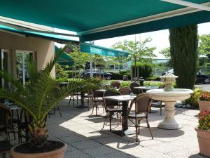 an outdoor patio with tables and chairs and a green umbrella at Charme Hotel en Beaujolais in Belleville-sur-Saône