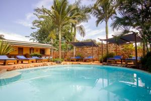 una piscina con mesas, sillas y palmeras en 2 Friends Guest House en Jinja