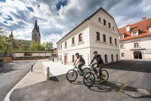 due persone in bicicletta di fronte a un edificio di Hostel Bearlog Kočevje a Kočevje