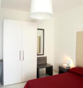 a white bedroom with a red bed and a mirror at Brezza Di Grecale in Trapani