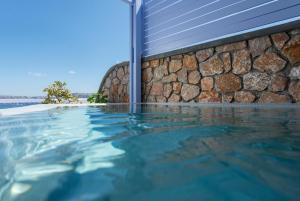 a swimming pool next to a stone wall at Earino Suites and Villa in Akrotiri