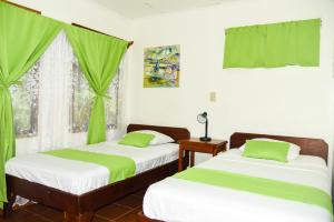 2 camas en una habitación con cortinas verdes y ventana en Hotel Marielos en Tamarindo
