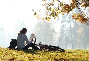 una mujer sentada en la hierba leyendo un libro al lado de una motocicleta en Centrale Hotel und Restaurant, en Waldkraiburg