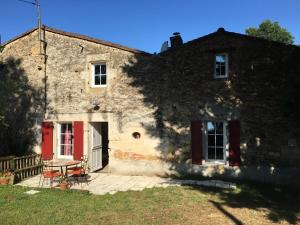una antigua casa de piedra con puertas rojas y un banco en Gite Le Puy Rabasteau, en Chantonnay