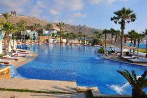 a large swimming pool with palm trees and a mountain at Pangea Beach Resort in Jiyeh