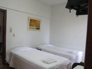 two beds in a room with white walls at Hotel Jaú in Jaú