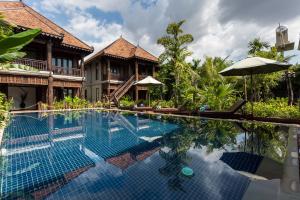 a swimming pool in front of a house with an umbrella at Java Wooden Villa & Residence in Siem Reap