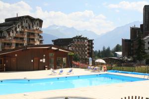 a swimming pool with chairs and mountains in the background at Résidence Grand Bois Clés Blanches in La Tania