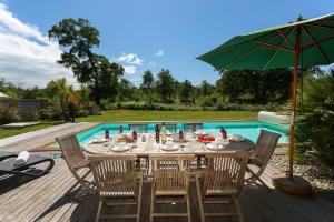 uma mesa com cadeiras e um guarda-sol ao lado de uma piscina em Madame Vacances Villas La Prade em Moliets-et-Maa