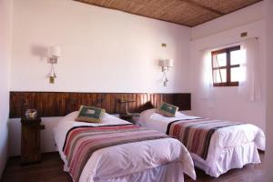 two beds in a room with white walls and a window at Hostal Montepardo in San Pedro de Atacama