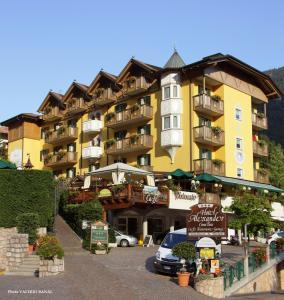 um grande edifício amarelo com carros estacionados num parque de estacionamento em Alexander Hotel Alpine Wellness Dolomites em Molveno