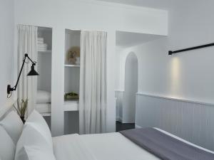 a white bedroom with a bed and a lamp at The Arches in Oia