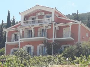 ein großes rosa Haus auf einem Hügel mit Bäumen in der Unterkunft Myrtos Hotel in Divarata