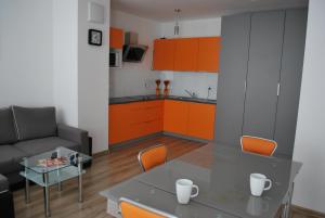 kuchnia ze szklanym stołem i pomarańczowymi szafkami w obiekcie Apart Morze apartamenty Vento we Władysławowie