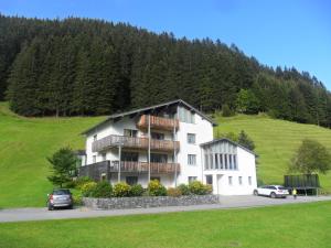 un grand bâtiment blanc avec des voitures garées devant lui dans l'établissement Ferienwohnungen Abel, à Damüls