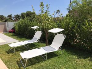 twee witte ligstoelen en een tafel in het gras bij Villetta San Leone in Agrigento