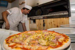 Ein Mann steht in einer Küche mit Pizza in der Unterkunft Rifugio Fermeda Hutte in St. Christina in Gröden