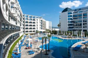 a resort pool with chairs and palm trees and buildings at Chaika Beach Resort in Sunny Beach