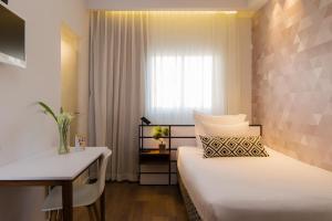 a bedroom with two beds and a desk and a window at Prima Tel Aviv Hotel in Tel Aviv
