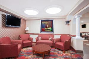 Ramada by Wyndham Edgewood Hotel & Conference Center في إدجوود: غرفة انتظار وكراسي حمراء وتلفزيون بشاشة مسطحة
