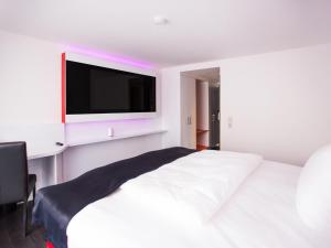 a bedroom with a white bed with a flat screen tv at DORMERO Hotel Villingen-Schwenningen in Villingen-Schwenningen