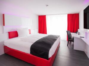 a bedroom with a large bed with red curtains and a desk at DORMERO Hotel Villingen-Schwenningen in Villingen-Schwenningen +18 photos