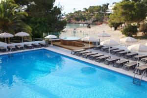 una piscina con sillas y sombrillas y una playa en Sandos El Greco - Adults Only, en Portinatx