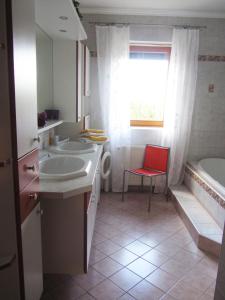 a bathroom with two sinks and a tub and a red chair at Anna's Home - Ferienwohnungen in Ratsch an der Weinstraße