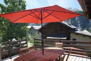 a wooden table with a red umbrella on a deck at le berger gourmand in Saint-Véran