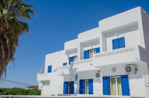 a white building with blue shutters and a palm tree at Hotel Delfini in Mylopotas