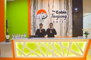 two men are standing behind a counter with a sign at The Cabin Tanjung Hotel Wonosobo in Wonosobo