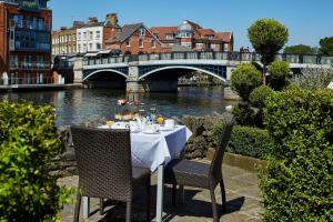 a table with chairs sitting next to a river with a bridge at Sir Christopher Wren Hotel in Windsor