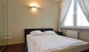 1 dormitorio con 1 cama con sábanas blancas y ventana en Żoliborz Apartamenty en Varsovia