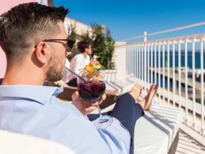un hombre sentado en un balcón sosteniendo una bebida en Nichotel, en Carloforte
