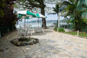 un patio con mesas, sillas y sombrillas cerca del océano en Pousada Vila Verde, en Porto Belo