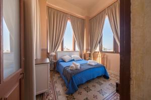 a bedroom with a bed with blue sheets and windows at Palazzo Vallebona in Gallipoli